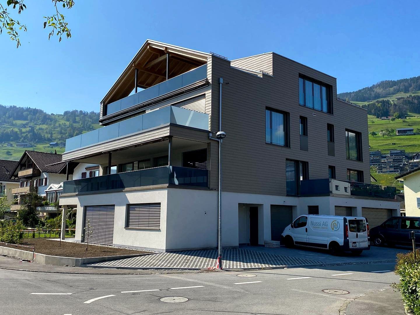 Mehrfamilienhaus mit Holzverkleidung und hellem Sockel, davor ein Lieferwagen mit Nussi-Beschriftung