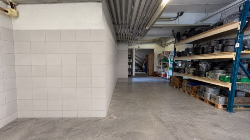 Hallenbereich mit weiss gefliester Wand links und Regalen voller Material rechts