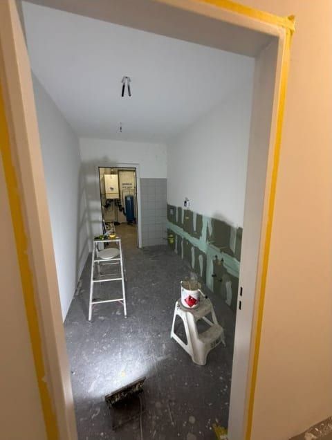 Blick durch eine Türzarge in einen neuen Raum, an der unteren Wandhälfte gespachtelte Stellen, eine Leiter und ein Eimer