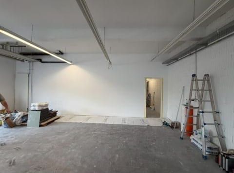 Heller, weiss gestrichener Raum mit Leuchten an der Decke, der Boden noch unbehandelt, Material und Leitern am Rand