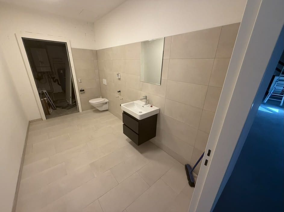 Fertiger WC-Raum mit wandhängendem WC, Lavabo auf dunklem Unterschrank, Spiegel und grossformatigen beigen Platten