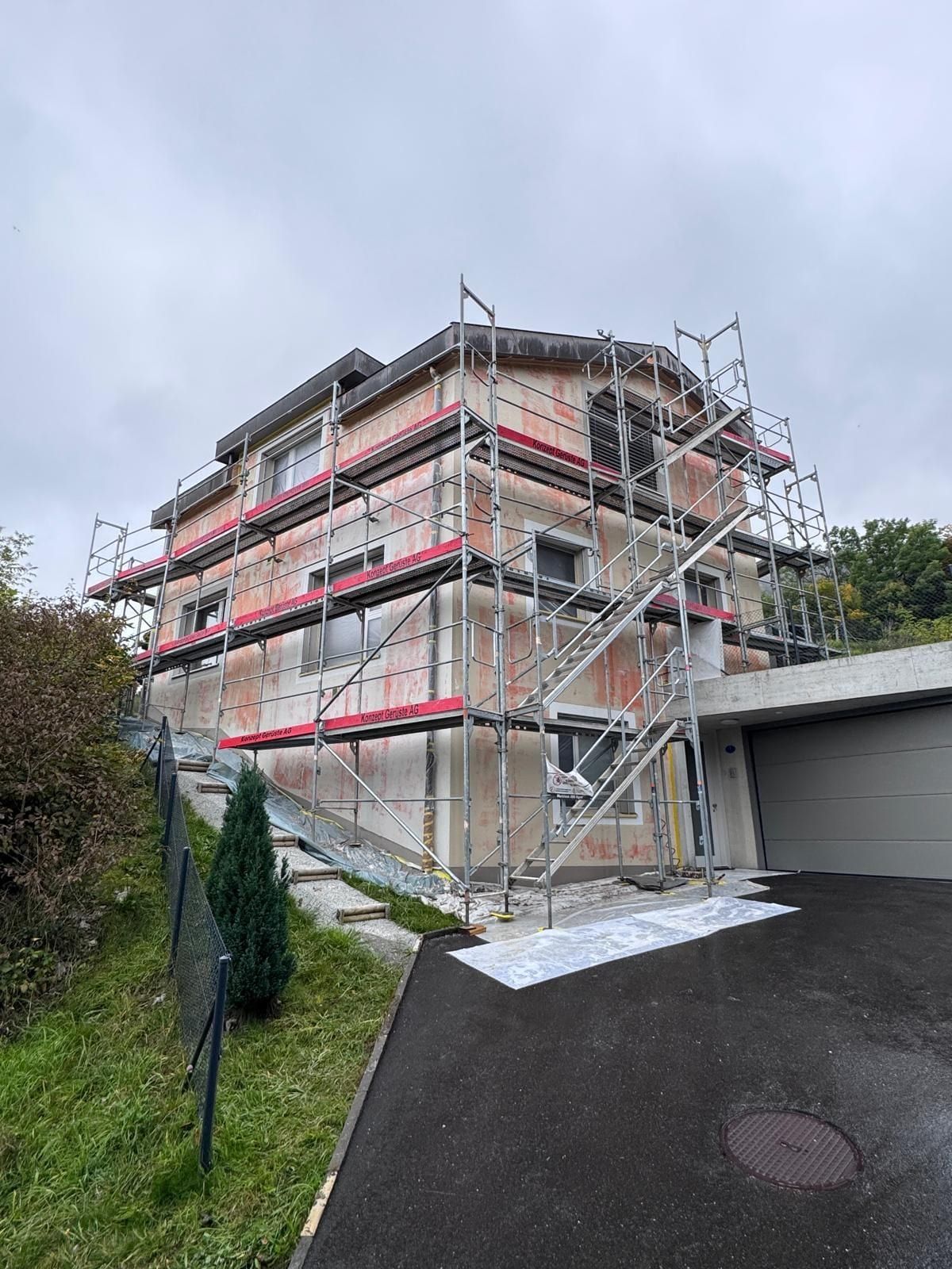 Mehrgeschossiges Haus im Gerüst, auf der Fassade rötliche ausgebesserte Stellen, am Boden Abdeckfolie