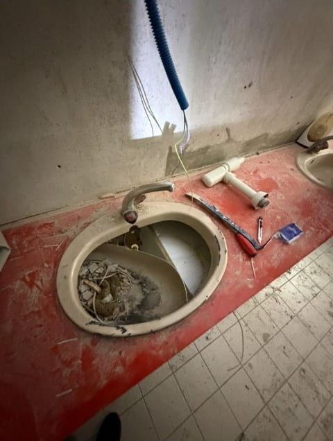 Eingebautes altes Lavabo voller Schutt in einer roten Abdeckung, darüber ein blaues Wellrohr mit Kabeln aus der Wand