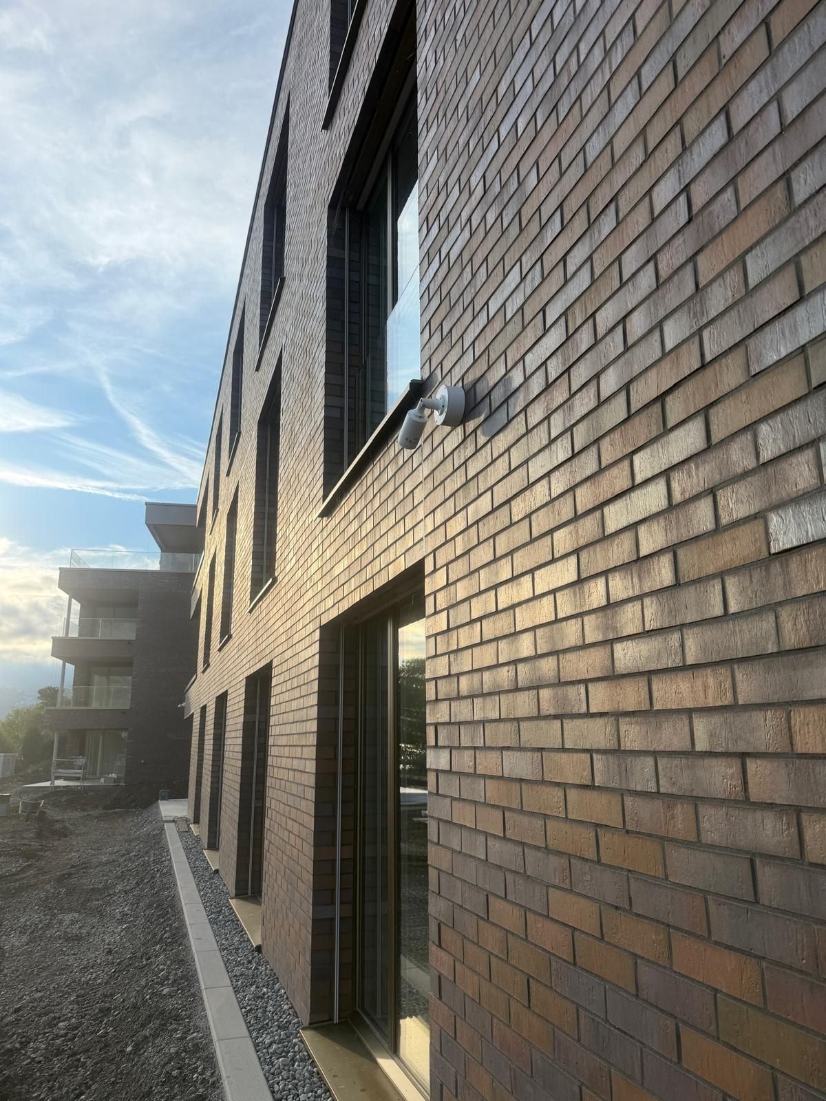 Neubau mit Fassade in Backsteinoptik und grossen Fenstern, davor ein Kiesstreifen